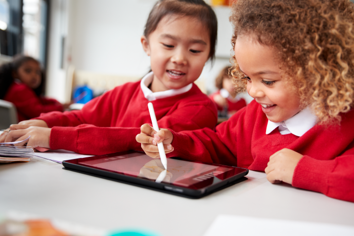 Two school girls in red uniform using a tablet device