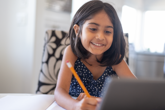 Child learning at home, in front of a computer screen, holding a pencil